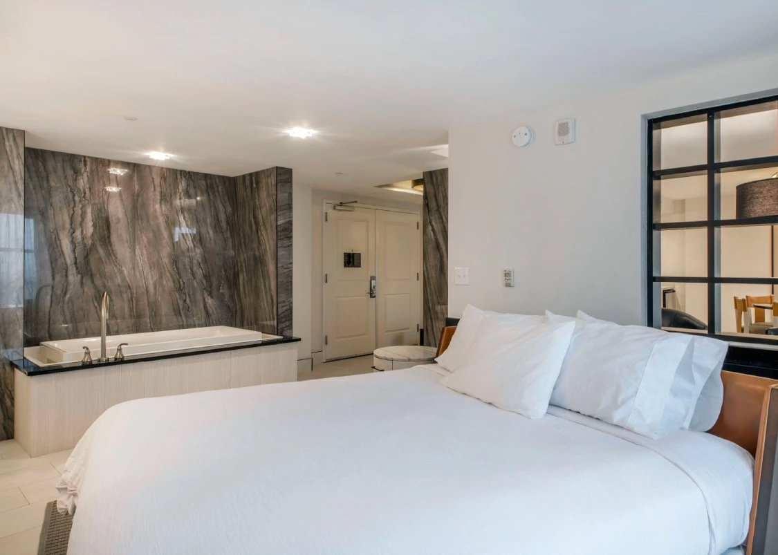 a hotel bed with white sheets and a bathtub in a room