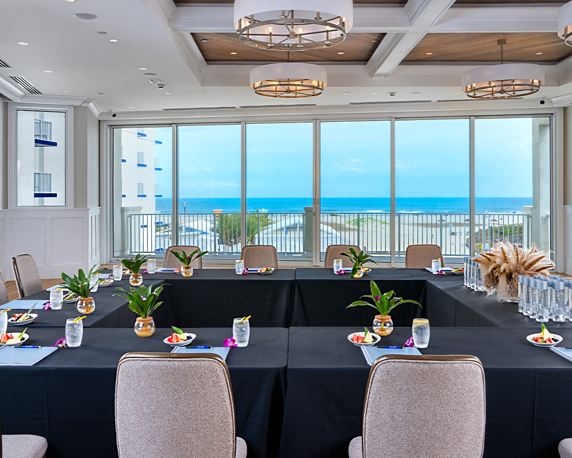 a room with tables and chairs with black tablecloths and a view of the ocean