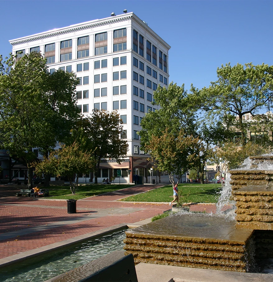 a fountain in a park with trees and a building in the background