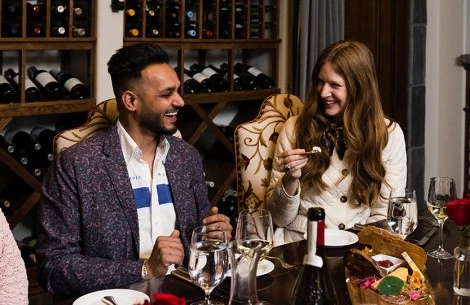 a man and woman sitting at a table with food and wine bottles