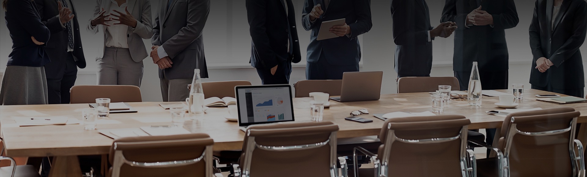 a group of people standing around a table with laptops and a tablet