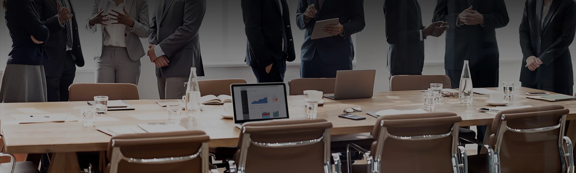 a group of people standing around a table with laptops and a tablet