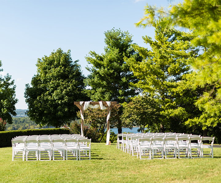 a wedding ceremony with white chairs and a wooden arch