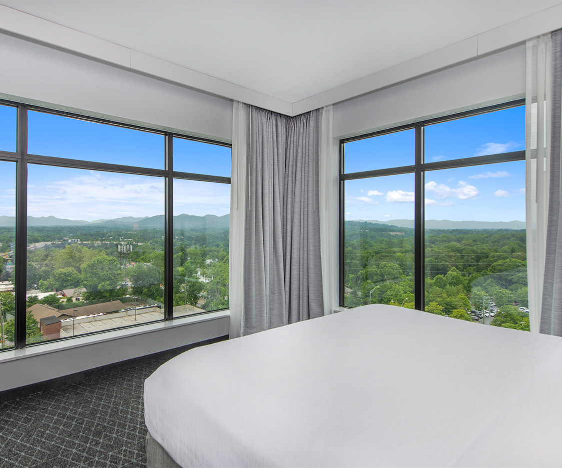 a bedroom with large windows and a view of trees