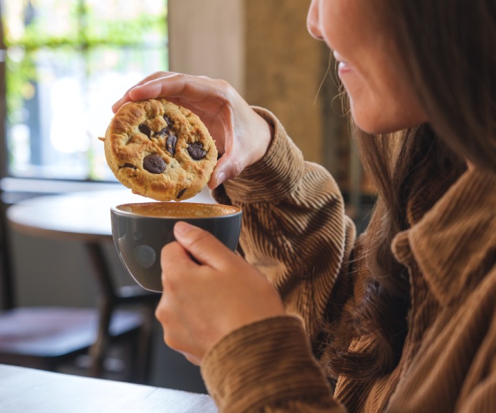 a woman holding a cookie and a cup of coffee