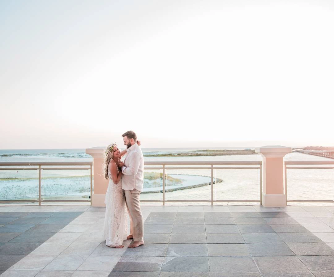 a man and woman standing on a patio with a railing and water in the background