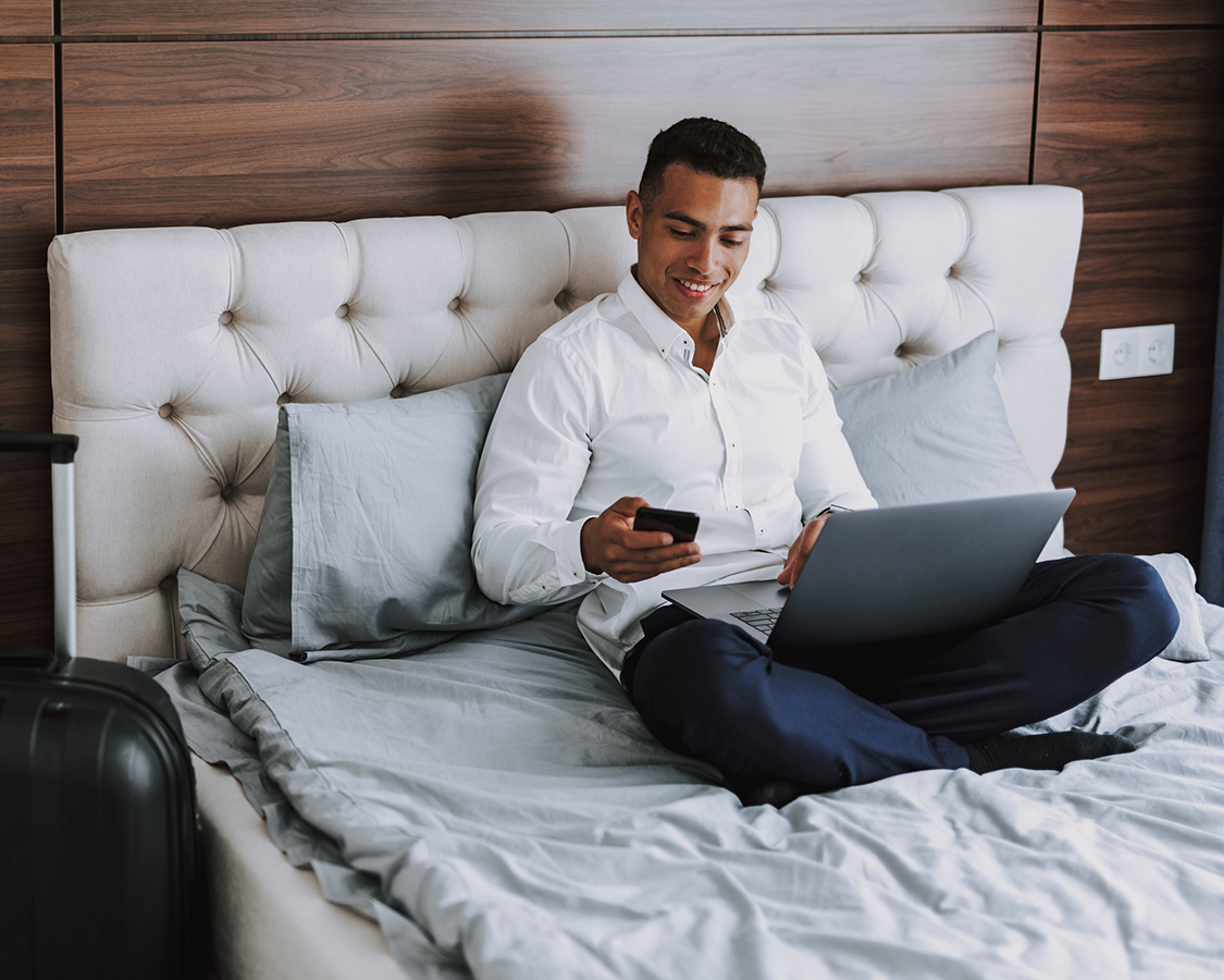 a man sitting on a bed using a laptop and phone