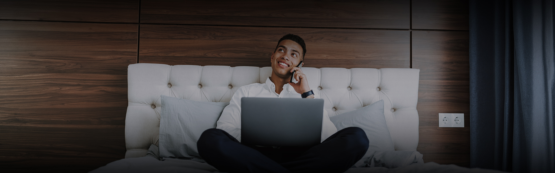 a man sitting on a bed with a laptop and phone