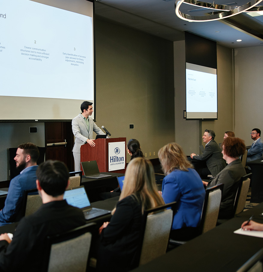a man standing at a podium with a projector screen in front of him