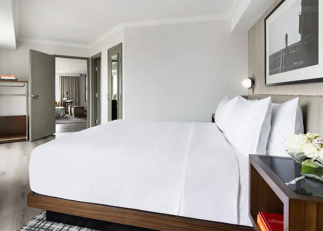 a bed with white sheets and a wood shelf