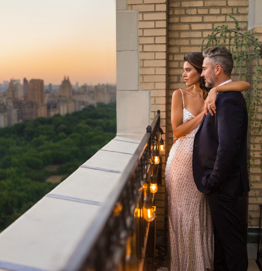 a man and woman standing on a balcony with a city in the background