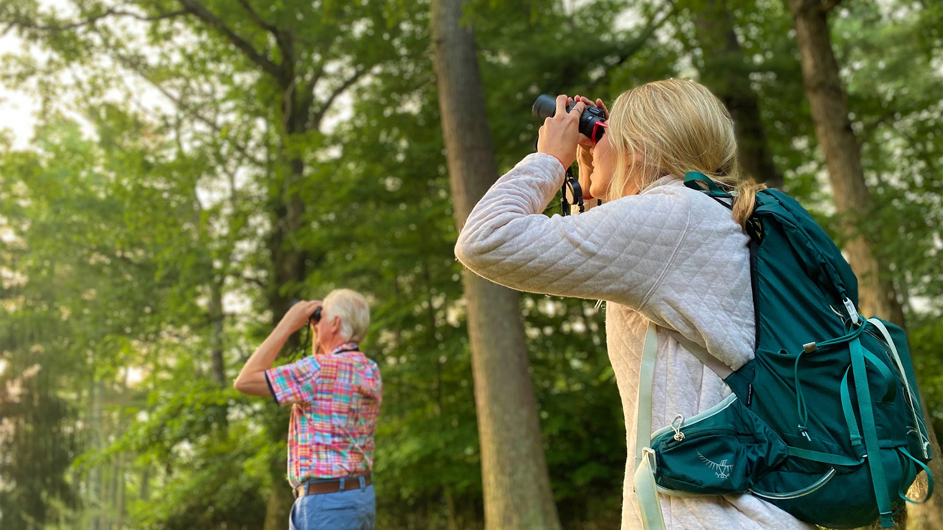 a woman looking through binoculars while a man looks through trees