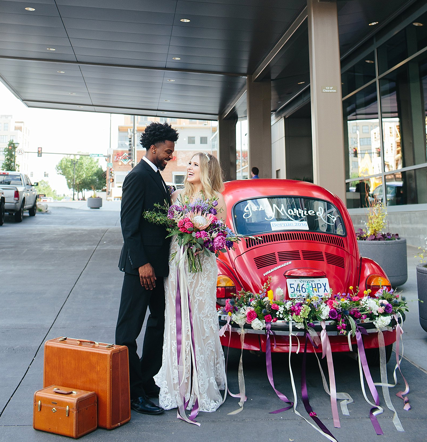 a man and woman standing next to a red car with flowers