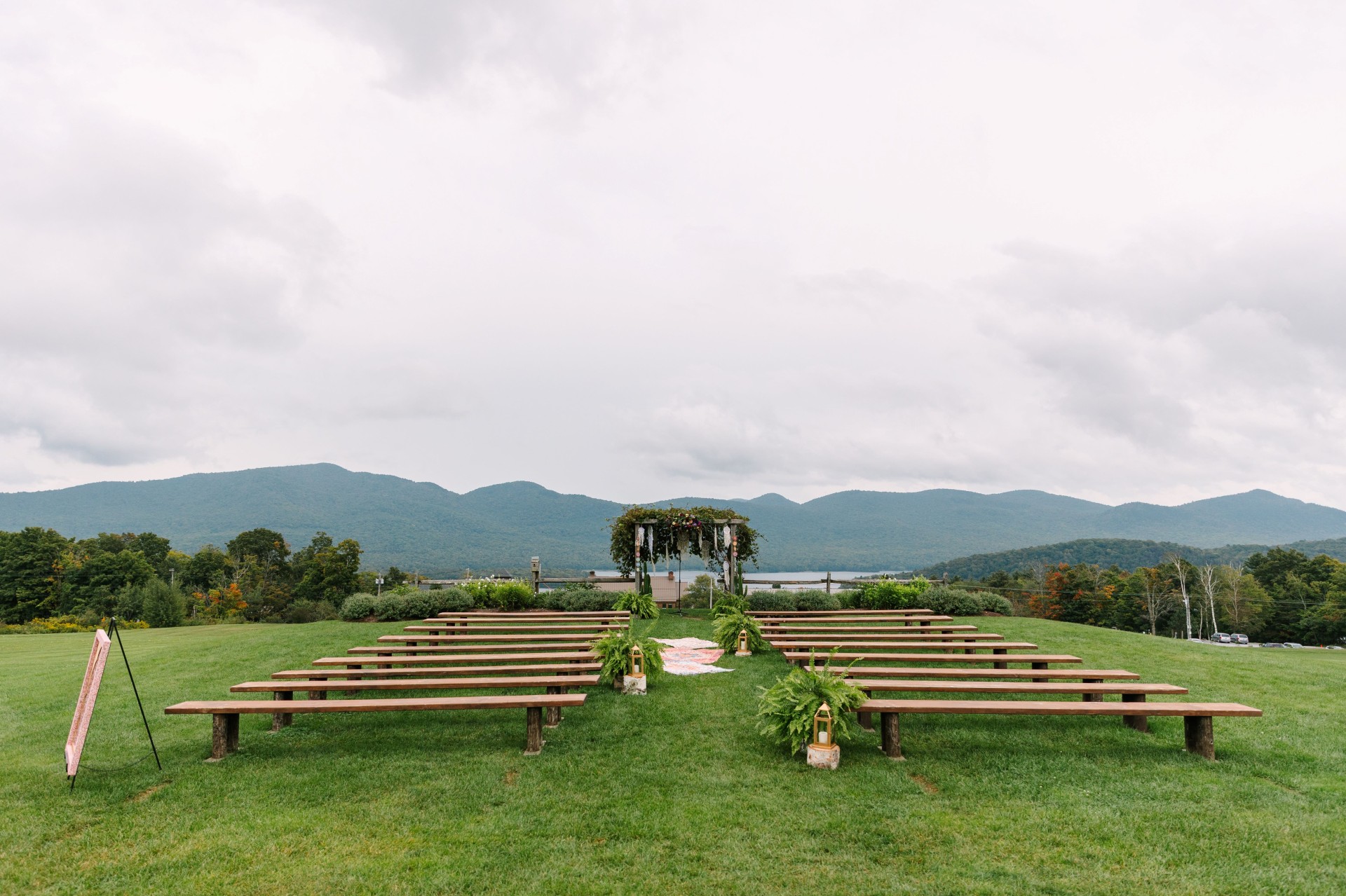 a wedding ceremony set up in a grassy area with benches and a white arch