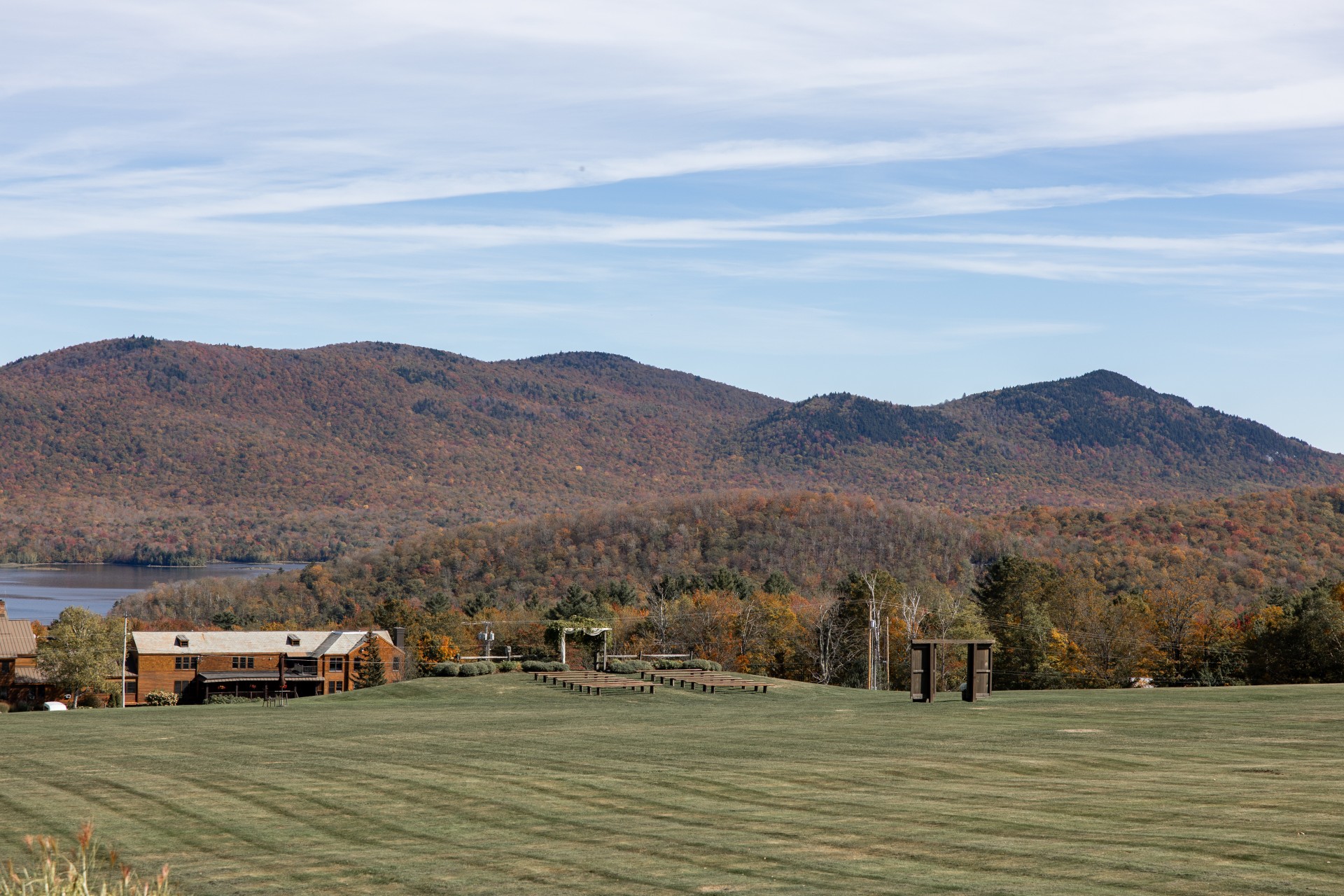 a large grassy field with trees and mountains in the background by Kate Seymour