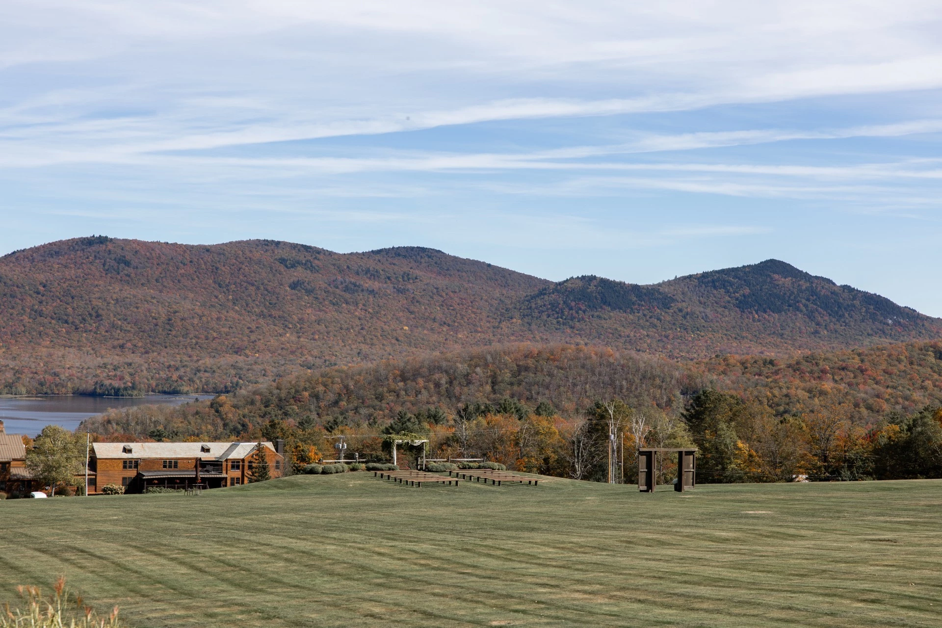 a large grassy field with trees and mountains in the background by Kate Seymour