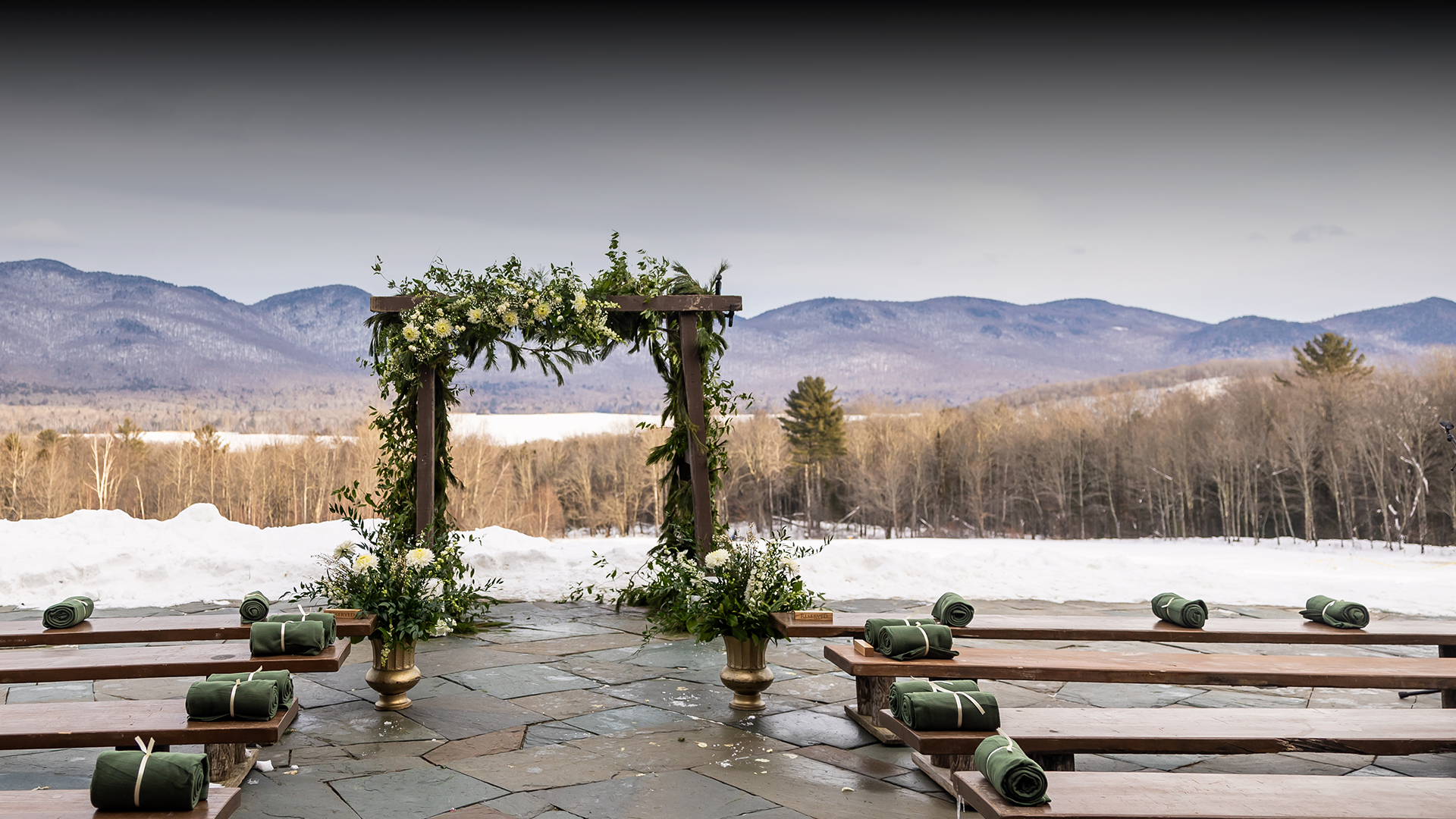 a wooden structure with flowers and benches in front of a snowy landscape