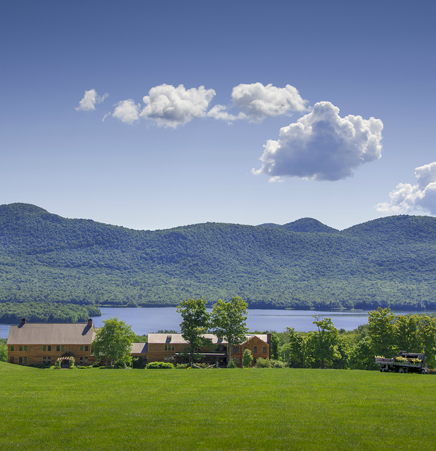 a house in a grassy field with a lake and mountains in the background