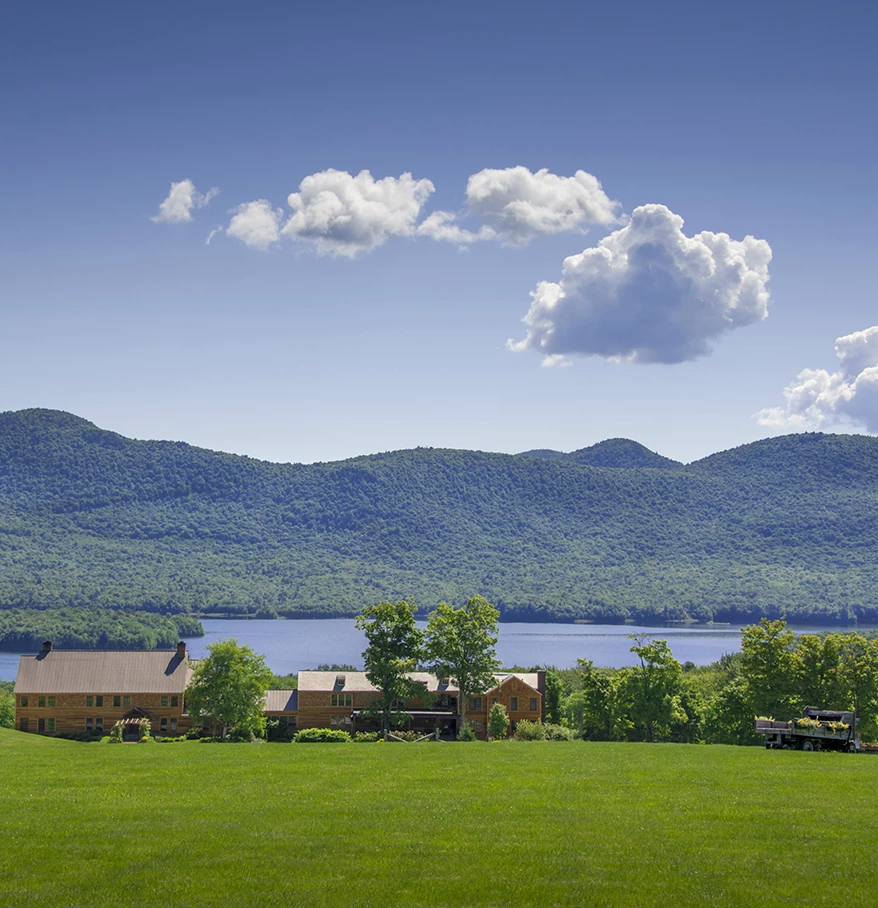 a house in a grassy field with a lake and mountains in the background