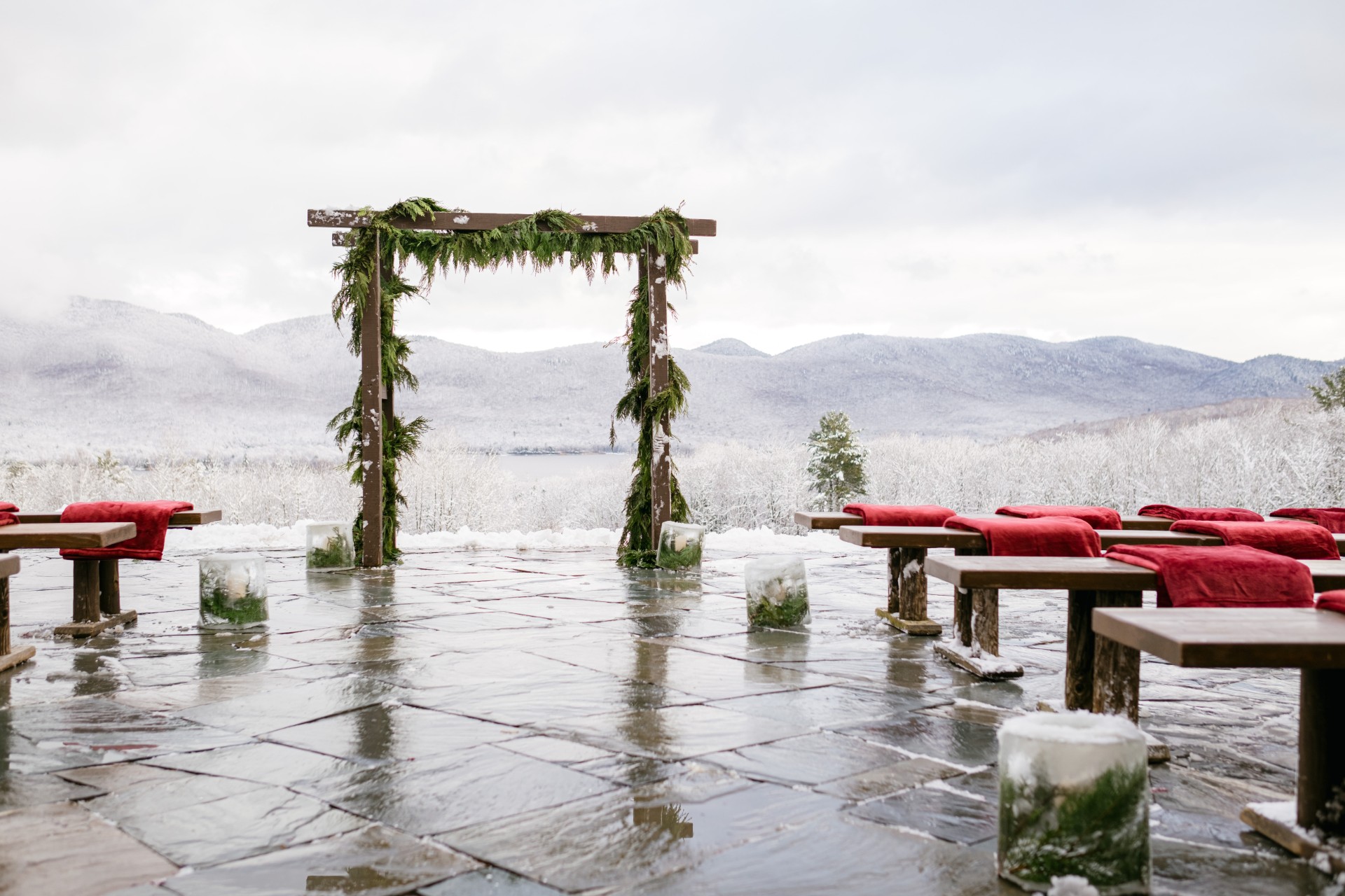a wooden structure with benches and red blankets on a snowy patio by Sixpence Studios