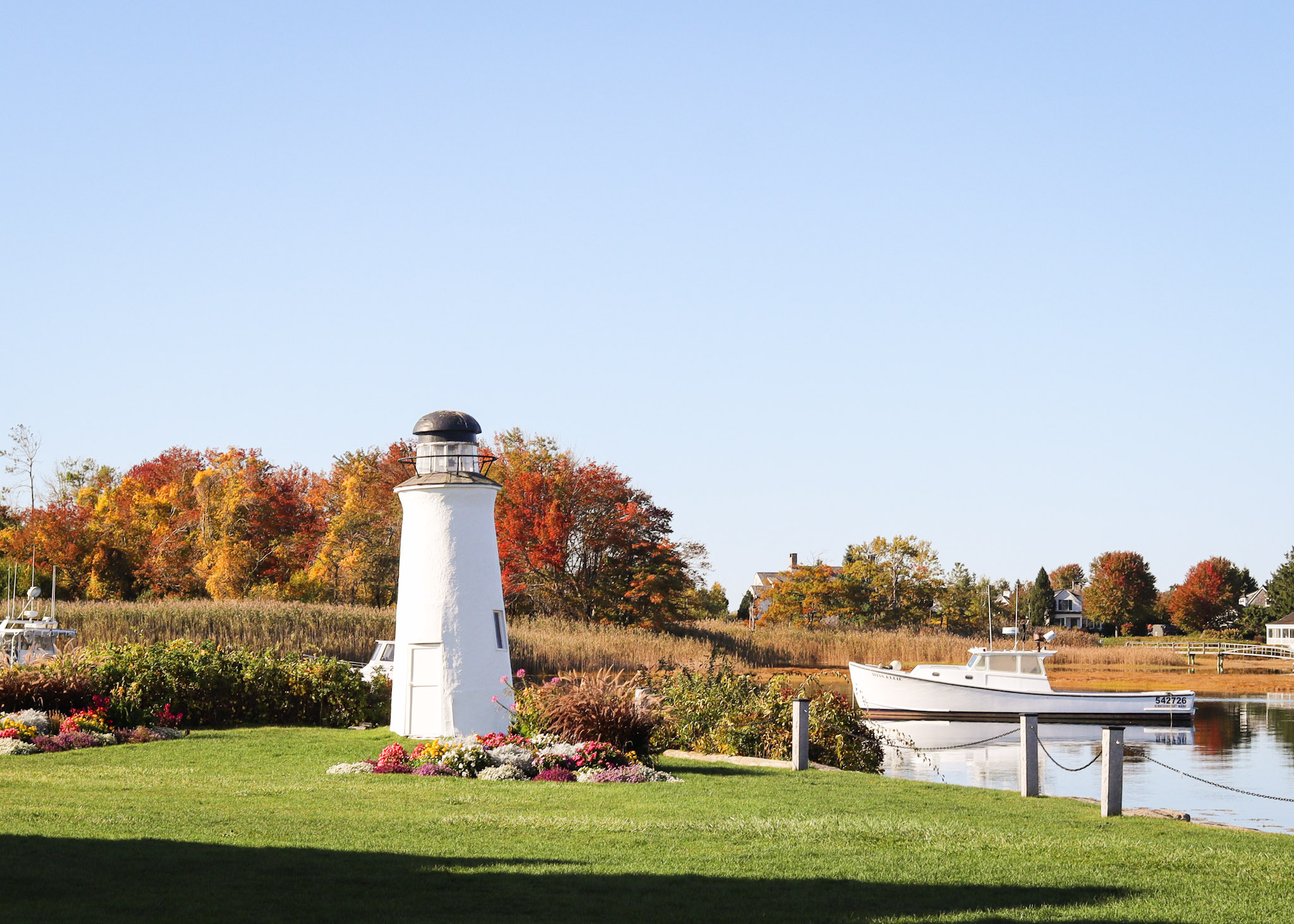 a lighthouse in a grassy area with a boat in the background