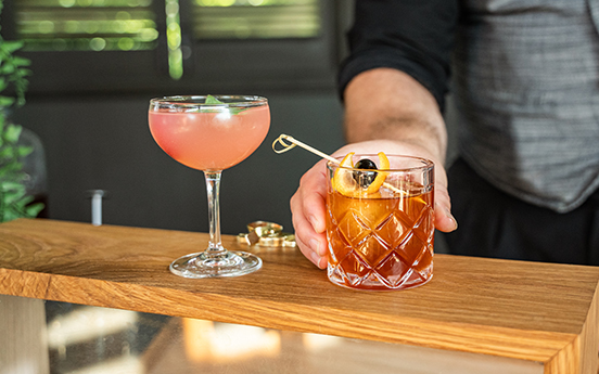 a hand holding a drink next to a glass of liquid