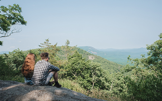 a man and woman sitting on a rock looking at a mountain
