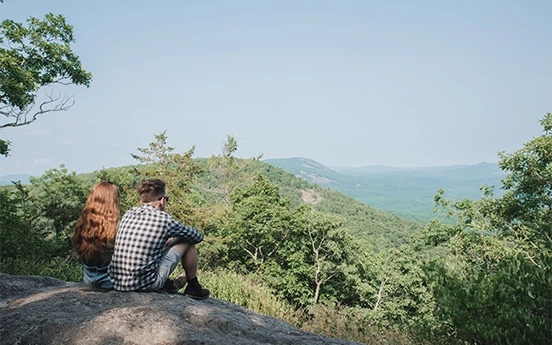 a man and woman sitting on a rock looking at a mountain