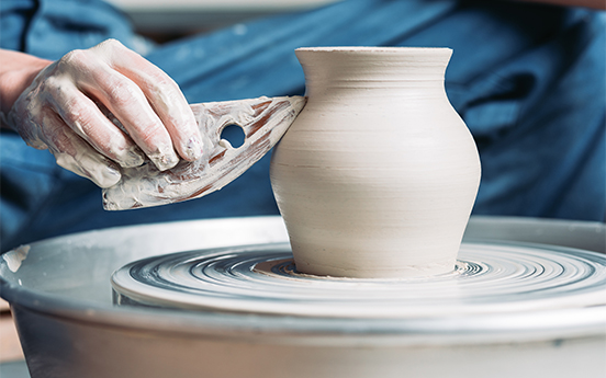 a person's hands painting a clay pot