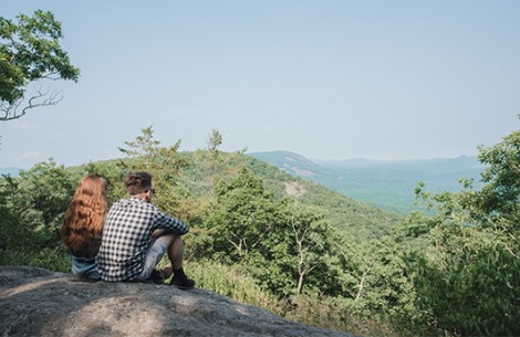 a man and woman sitting on a rock looking at a valley