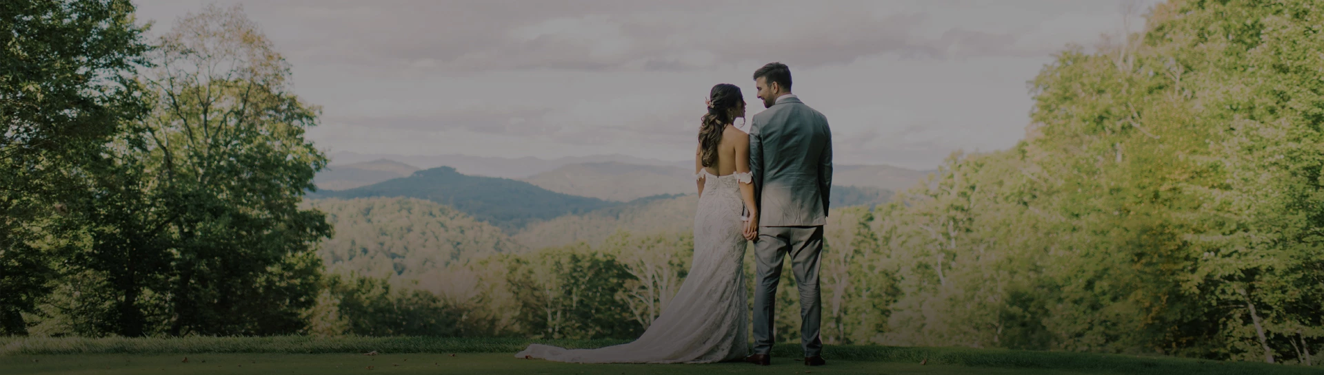 a man and woman standing on grass with mountains in the background