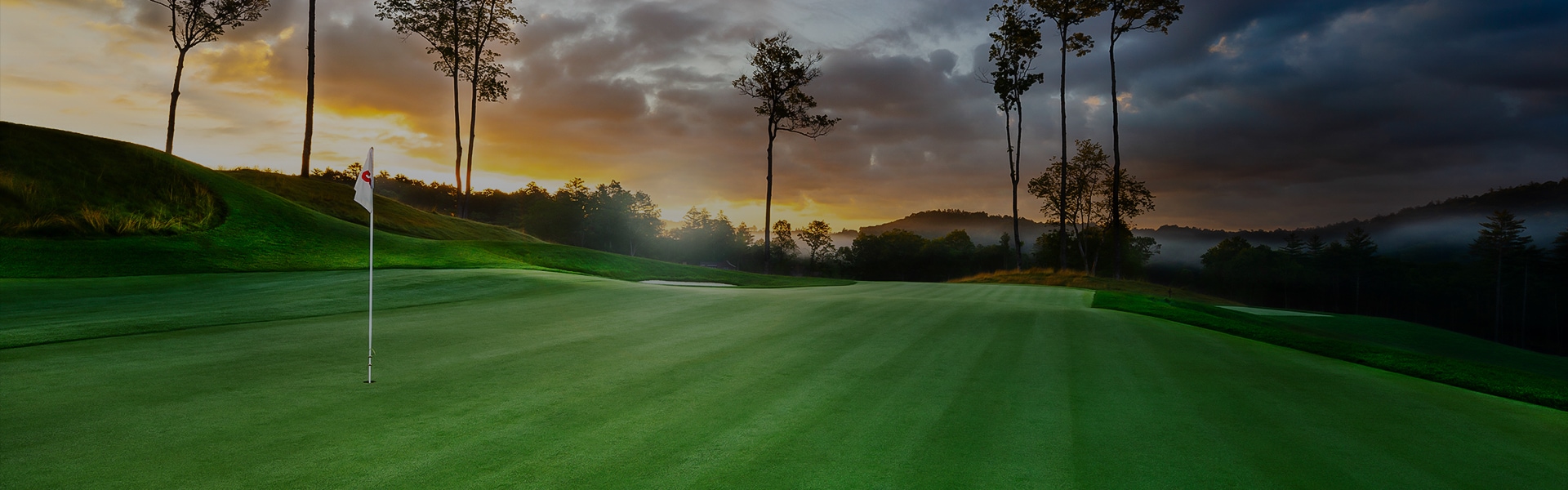 a golf course with trees and a sunset