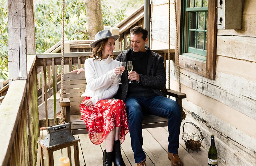 a man and woman sitting on a swing with wine glasses
