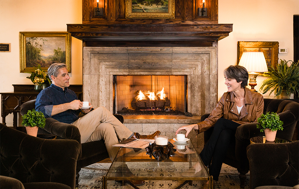 a man and woman sitting in chairs by a fireplace