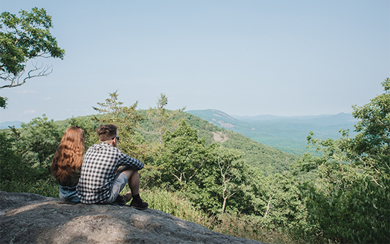 a man and woman sitting on a rock looking at a valley