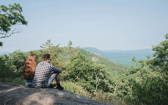 a man and woman sitting on a rock looking at a valley