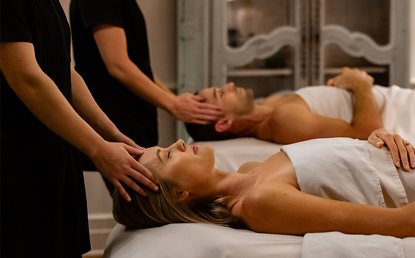 a man and woman lying on bed with hands on head