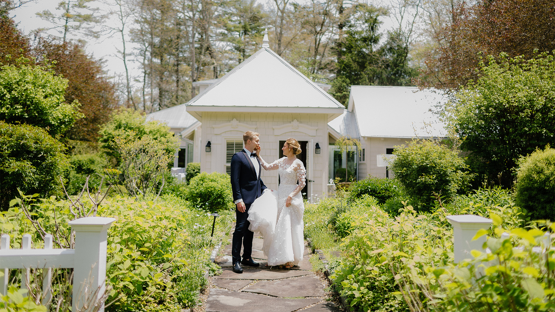 a man and woman in wedding attire standing on a path in front of a house