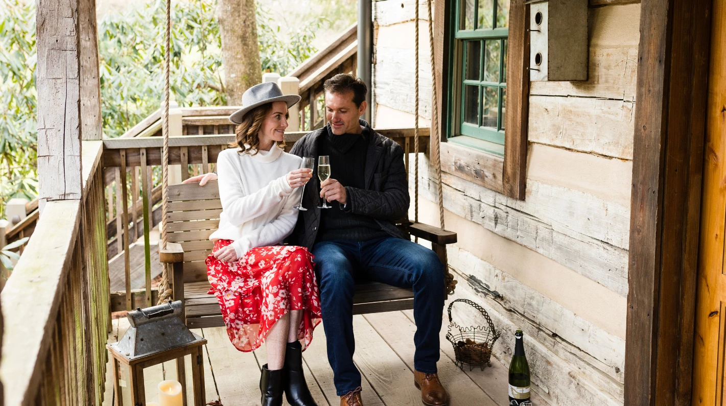 a man and woman sitting on a swing with wine glasses