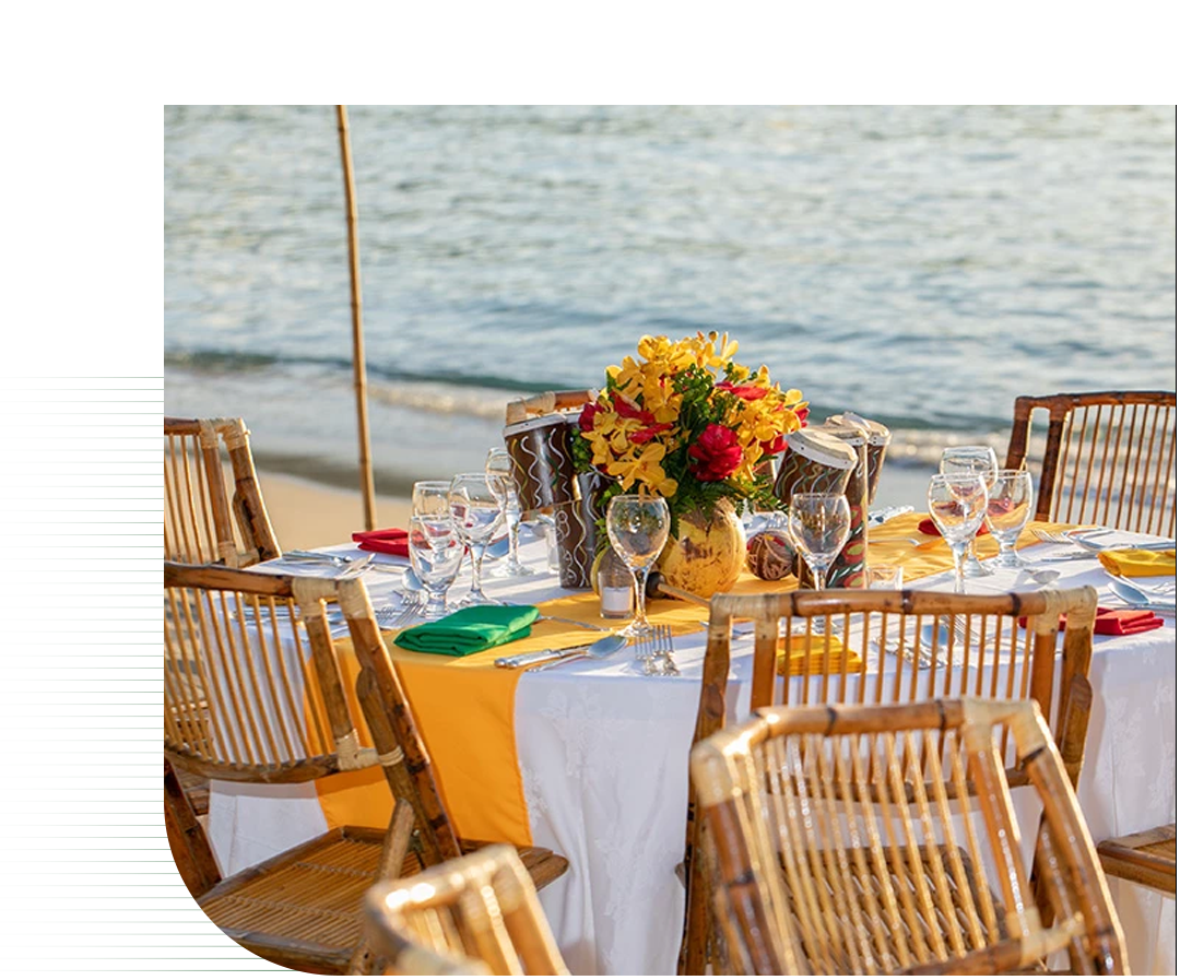 a table set for a dinner with a bouquet of flowers and wine glasses on a beach