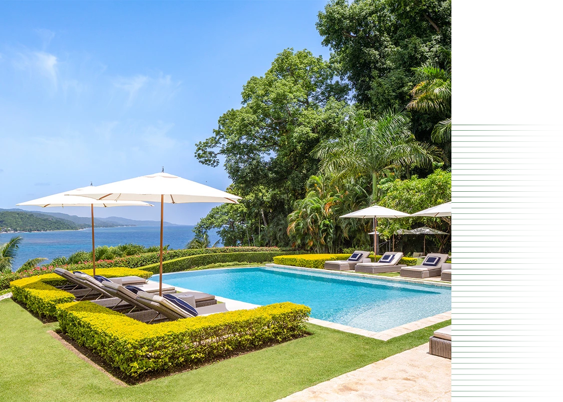 a pool with lounge chairs and umbrellas by a body of water