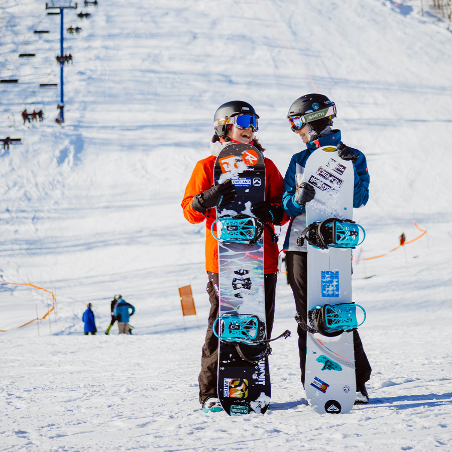 two people standing in the snow with their snowboards