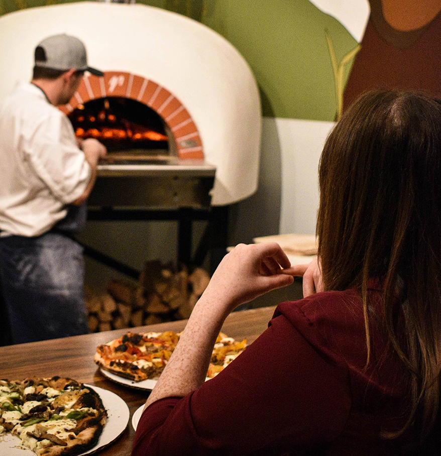 a woman sitting at a table with plates of pizza