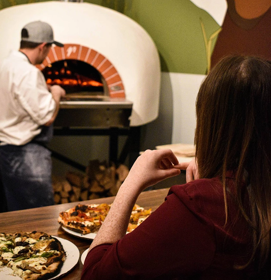 a woman sitting at a table with plates of pizza