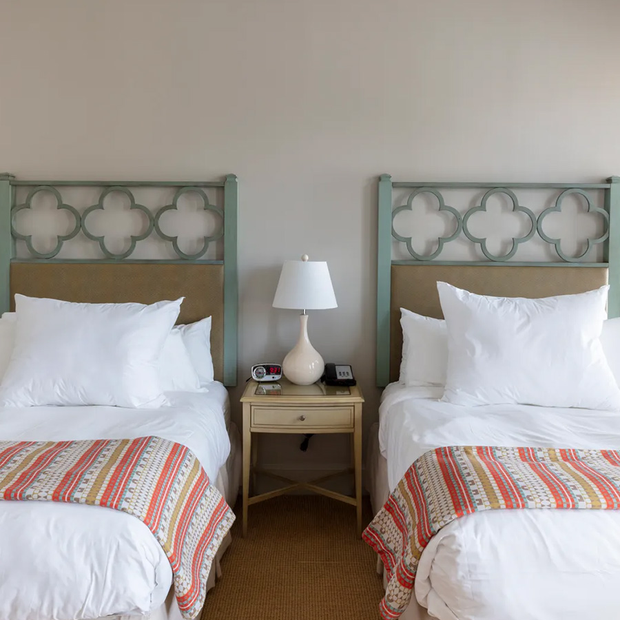 two beds with pillows and a lamp on a nightstand