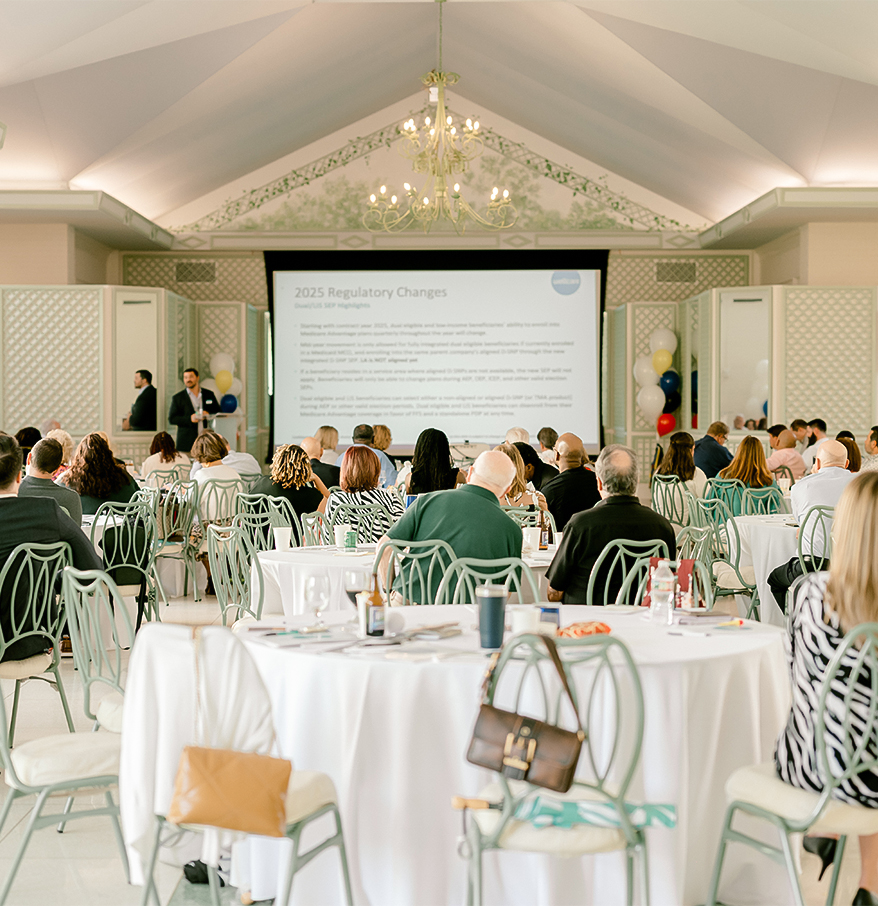 a group of people sitting at tables in a room with a projector screen