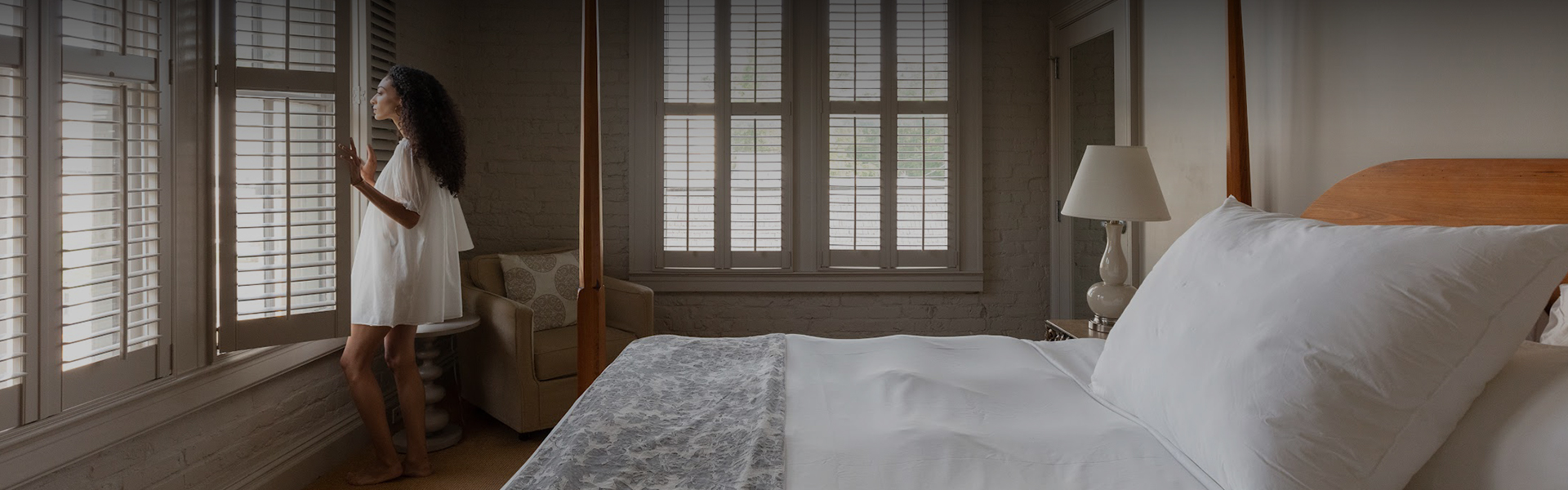 a bed with a white sheet and a wooden pole in a room with windows