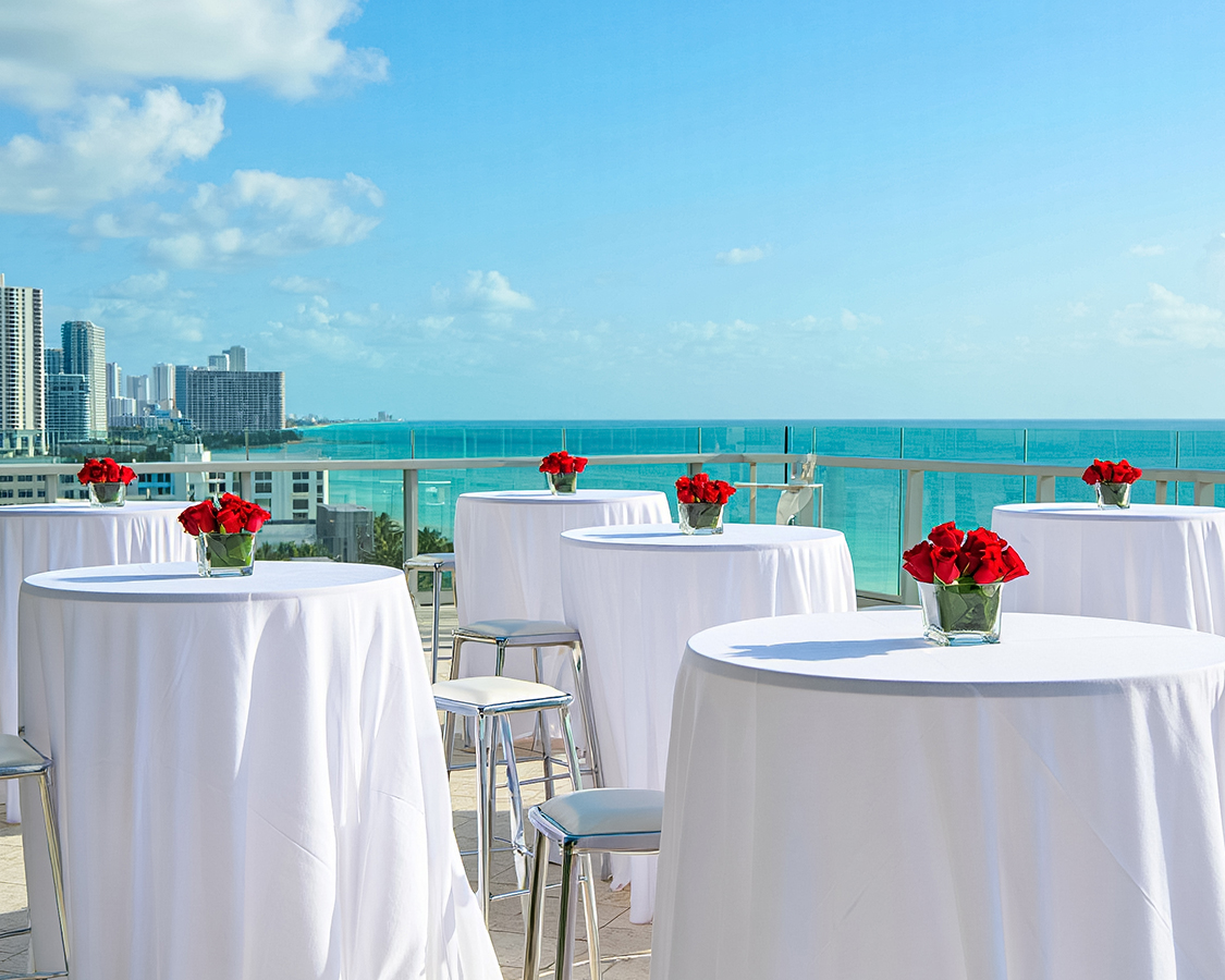 a table set up with white tables and red flowers on it