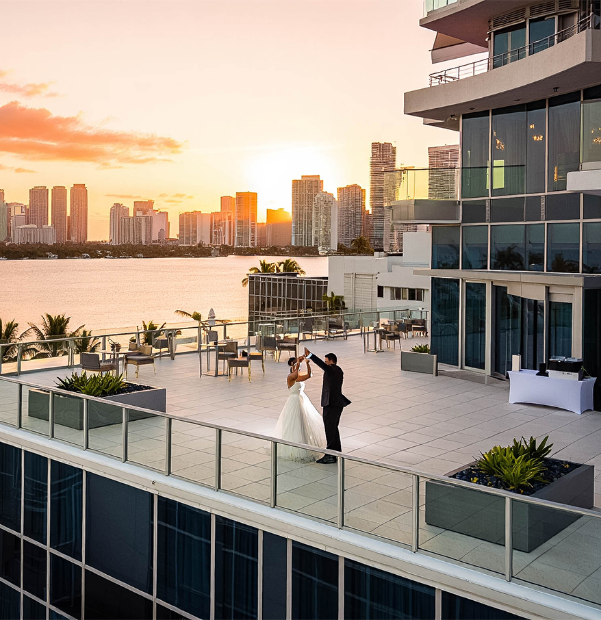 a man and woman dancing on a rooftop overlooking a body of water