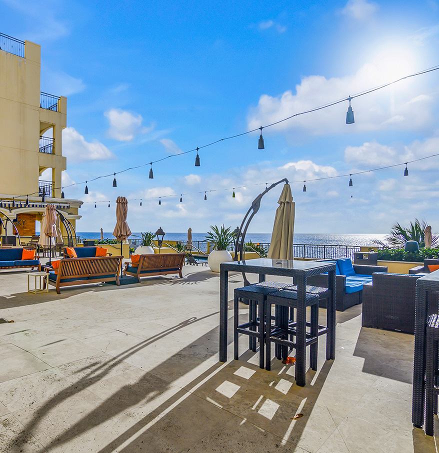 a patio with chairs and umbrellas and a building with a body of water in the background